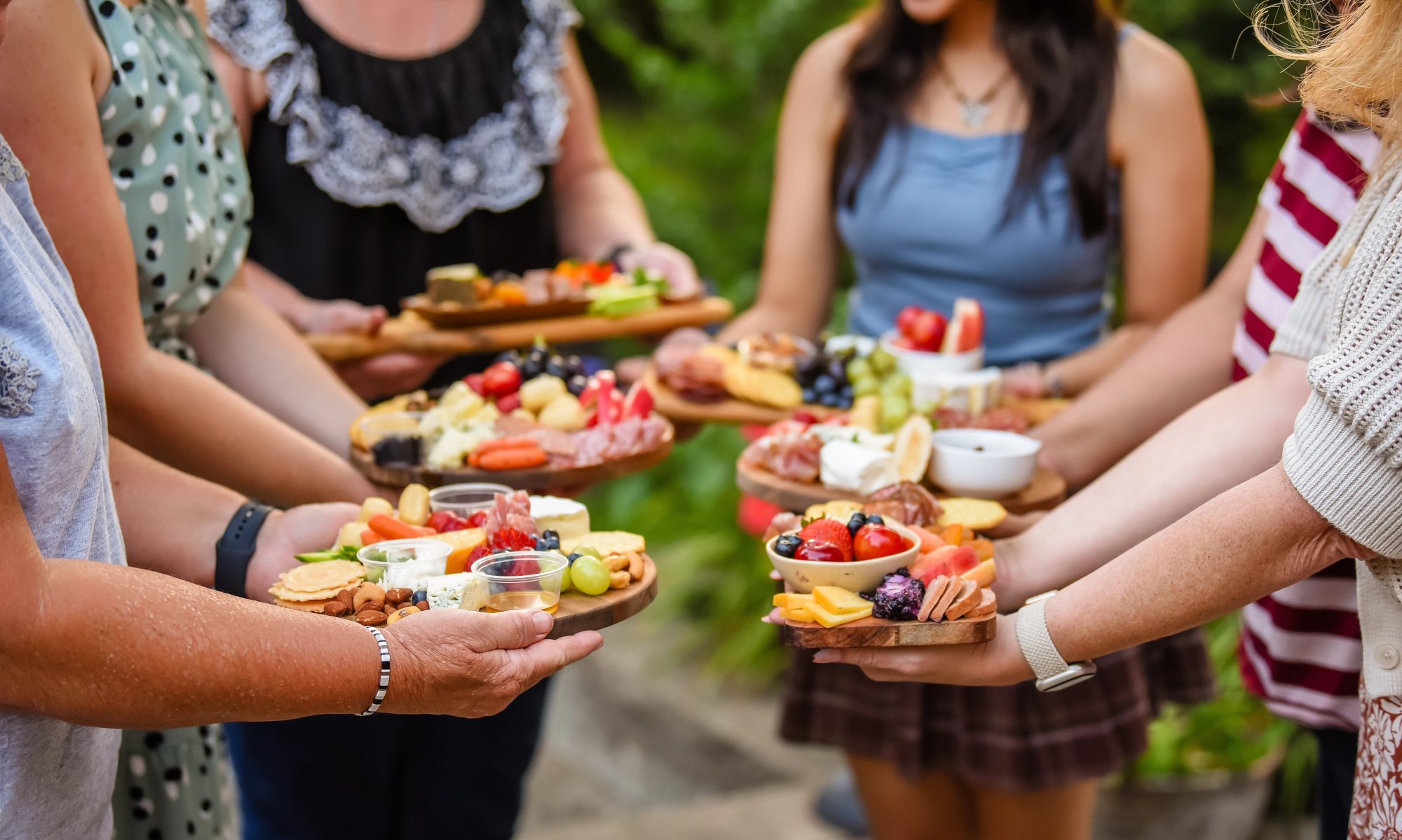 A group of people, standing in a circle, holding out their charcuterie boards.